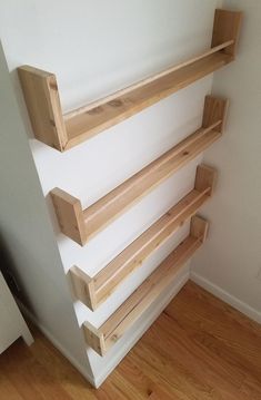 three wooden shelves mounted to the side of a white wall next to a wood floor