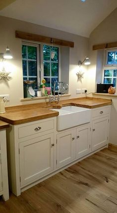 a kitchen with white cabinets and wooden counter tops in front of two windows that look out onto the woods