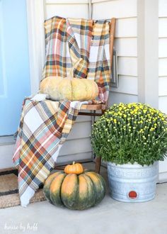 pumpkins and gourds are sitting on the front porch with plaid blankets over them