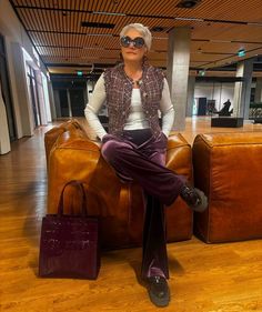 a woman sitting on top of a brown leather chair in an airport lobby with her legs crossed