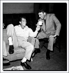 two men are sitting on a couch drinking from mugs while another man sits in the chair