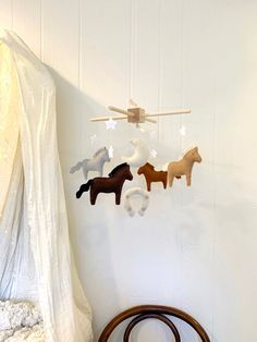 three wooden horses hanging on a white wall next to a round chair and table in front of a curtain