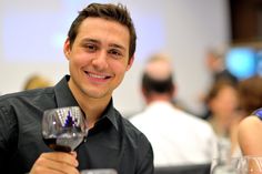 a man sitting at a table with a glass of wine in his hand and smiling