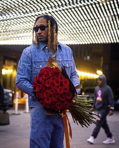 a man with dreadlocks holding a bouquet of red roses in front of a building