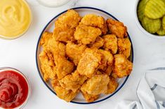 a plate full of fried chicken next to two bowls of pickles and ketchup