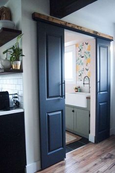 an open door leading to a kitchen with wood floors and white walls, in front of a sink