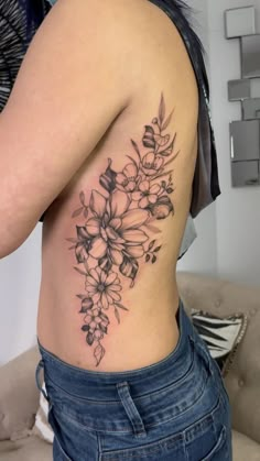 a woman's lower back tattoo with flowers and leaves on her left side ribcage