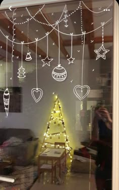 the reflection of a christmas tree in a window with lights hanging from it's sides