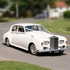 a white car is driving down the street in front of some grass and trees,