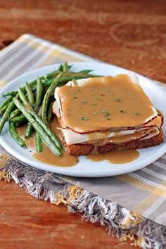 a white plate topped with green beans covered in gravy next to a sandwich