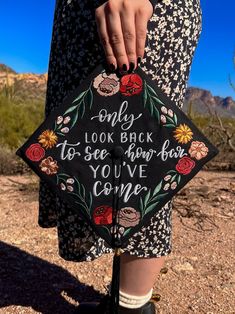 a woman is holding a black graduation cap with flowers on it that says, only look back to see how far you've come