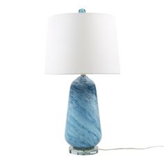 a blue glass table lamp with a white shade on the base and a light bulb plugged in