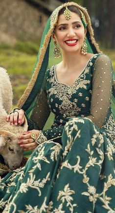 a woman in a green and gold wedding dress is petting a sheep