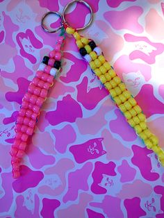 two pink and yellow beaded keychains are on a camouflage print tablecloth