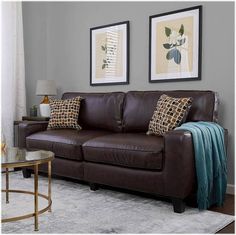 a living room with two framed pictures on the wall and a brown leather couch in front of it