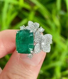 a close up of a person's hand holding an emerald and diamond ring