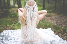 a woman sitting on top of a white blanket in the woods wearing a headpiece