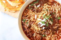 a bowl of beef noodle soup with bread on the side