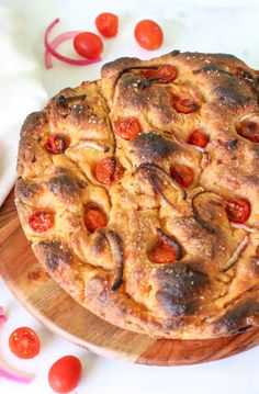 a pizza sitting on top of a wooden cutting board next to sliced onions and tomatoes