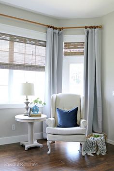 a white chair sitting in front of a window next to a table with a lamp on it