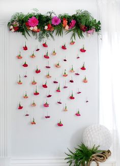 a white wall with pink flowers hanging from it's sides and greenery on the side