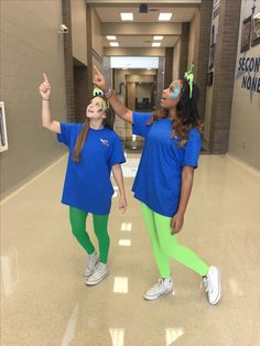 two girls in blue shirts and green leggings are standing on the floor with their hands up