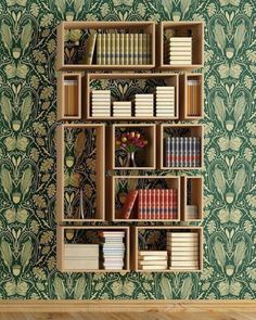 a bookshelf filled with lots of books in front of a wallpapered wall