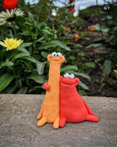 two clay animals sitting next to each other on top of a stone slab in front of flowers