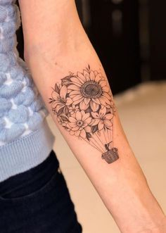 a woman with a tattoo on her arm holding a hot air balloon filled with sunflowers