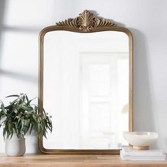 a mirror sitting on top of a wooden table next to a potted plant and bowl