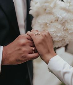 the bride and groom are holding hands with their wedding rings on their fingers while they hold each other's hand