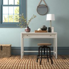 a desk with a lamp, vases and other items on it in front of a window