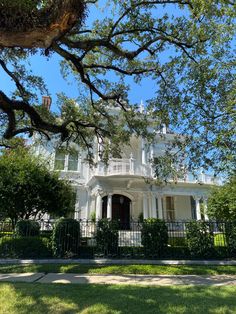 a large white house sitting on the side of a lush green field next to trees