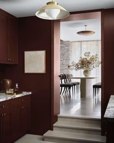 a kitchen with red walls and marble counter tops, along with stairs leading up to the dining room