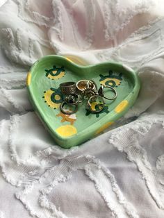 a heart shaped tray filled with lots of rings on top of a white cloth covered bed