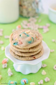 a stack of cookies with sprinkles on a white plate next to a glass of milk