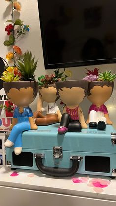 three people sitting on top of a suitcase with plants in their heads and flowers growing out of them