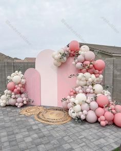 an outdoor area with balloons and flowers on the ground, in front of a pink wall