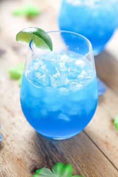 a blue drink with ice and mint garnish on the rim, sitting on a wooden table