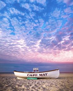 a boat sitting on top of a sandy beach under a cloudy blue and pink sky