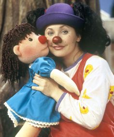 a woman holding a doll in her arms with a clown nose on it's cheek