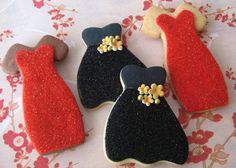 three decorated cookies with black and red dresses on them sitting on a floral tablecloth