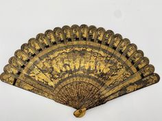 an old fan is sitting on a white surface with gold trimmings and designs