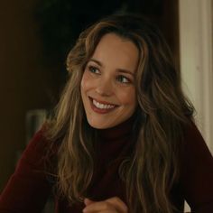 a woman with long hair smiling and wearing a red turtle neck sweater in front of a doorway