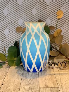 a blue and white vase sitting on top of a wooden floor next to plants in front of a wall