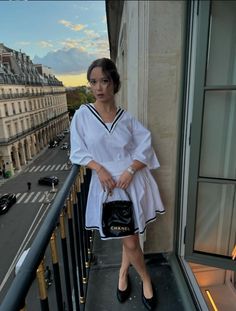 a woman is standing on the balcony with her hand in her purse and looking at the camera