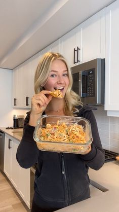 a woman holding a glass dish with food in it while standing next to a kitchen counter