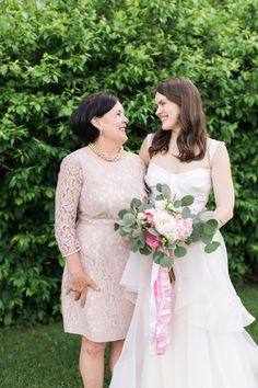 two women standing next to each other in front of bushes