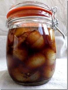 a jar filled with onions sitting on top of a white cloth covered table next to a red lid