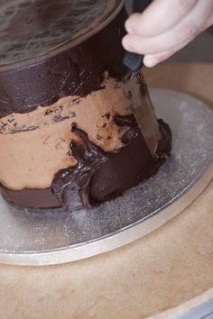 a person cutting into a chocolate cake on top of a metal platter with a knife